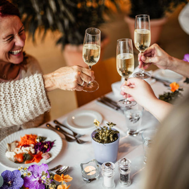 Drei Gläser Sekt werden in einem festlich gedeckten Tisch mit buntem Essen und Blumen in Töpfen angestoßen