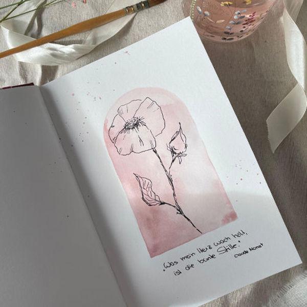 Offenes Skizzenbuch mit einer zarten Blumenzeichnung auf rosafarbenem Hintergrund, daneben Pinsel und Wasserglas