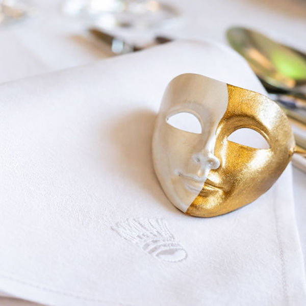 Eine goldene, dekorative Theatermaske liegt auf einer weißen Stoffserviette