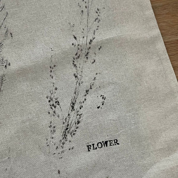 Stoff mit zartem Pflanzenabdruck in Schwarz und dem Schriftzug ‘Flower’