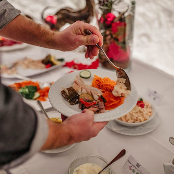 Eine Person hält einen Teller in der Hand. Auf diesem Teller sind verschiedene Vorspeisen (Lachs, Fisch und Brot sowie Karottensalat). Die Person tut sich Meerrettich mit einem Löffel auf.